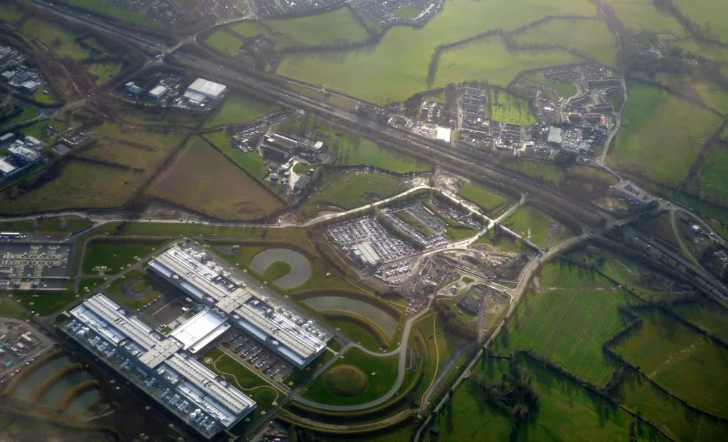 Aerial view of a large data center campus beside green fields and a motorway